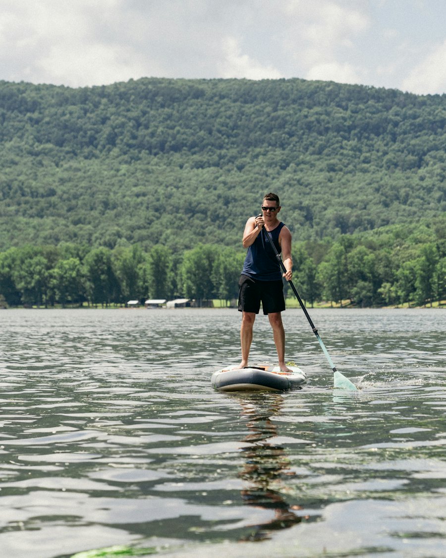 A man on a paddleboard on a lake in front of green hills